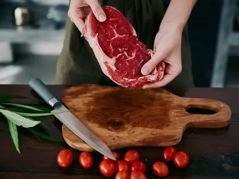 Руки повара держат кусок сырого мяса над деревянной доской
