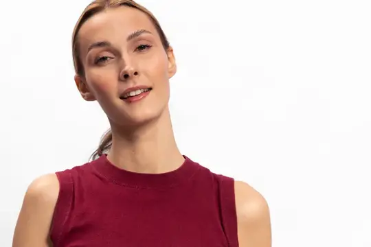 Молодая женщина с улыбкой в бордовой майке на белом фоне