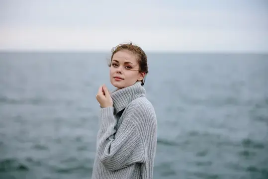 Молодая женщина в сером свитере на фоне холодного моря