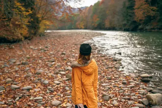 Женщина в жёлтой куртке путешествует по осеннему лесу, реке и горам