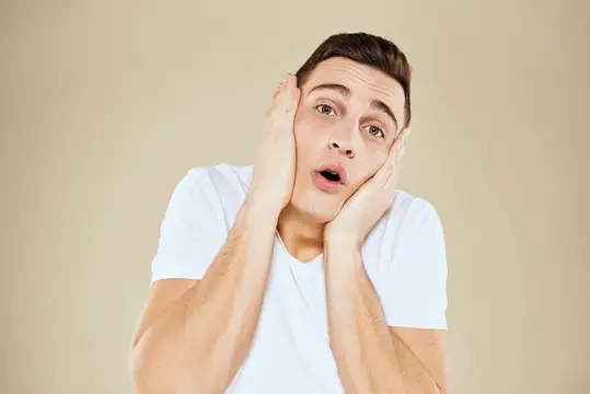Удивлённый молодой мужчина в белой футболке схватился за голову