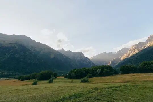 Горный пейзаж с зелёной долиной и скалистыми хребтами в лучах солнца