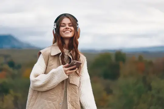 Улыбающаяся девушка в наушниках со смартфоном на фоне осенних гор