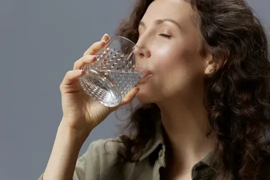 Кудрявая женщина с закрытыми глазами пьёт воду из гранёного стакана