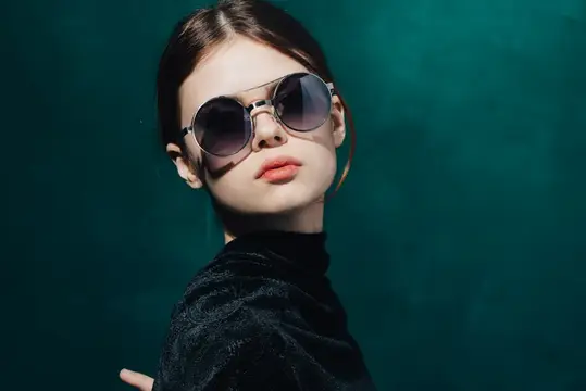 Женщина на зеленом фоне в черном свитере и солнцезащитных очках, макияж
