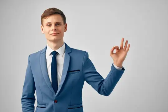 Молодой мужчина в синем костюме показывает жест «всё отлично»