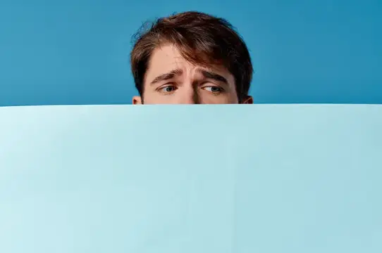 Испуганный мужчина выглядывает из-за светло-голубой панели