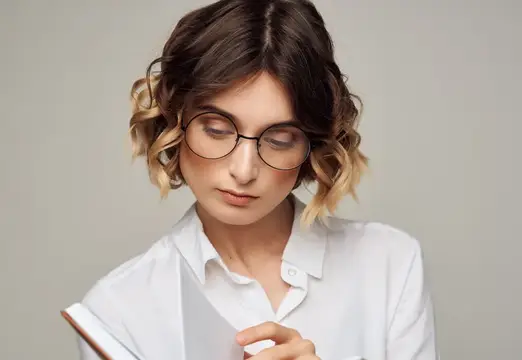 Молодая женщина с волнистыми волосами в очках читает книгу