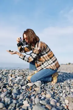 Девушка фотографирует камни на галечном пляже