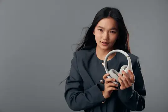 Портрет молодой девушки, держащей полноразмерные наушники руками на сером фоне