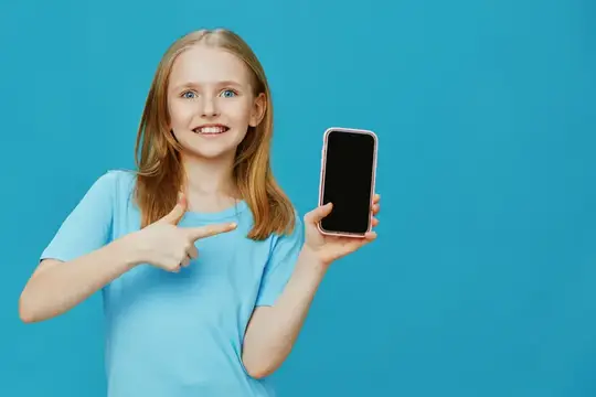 Счастливая девочка в голубой рубашке с восторгом указывает на смартфон на фоне ярко-голубого фона, передавая радостную и увлекательную атмосферу, идеально подходящую для рекламы цифровых продуктов