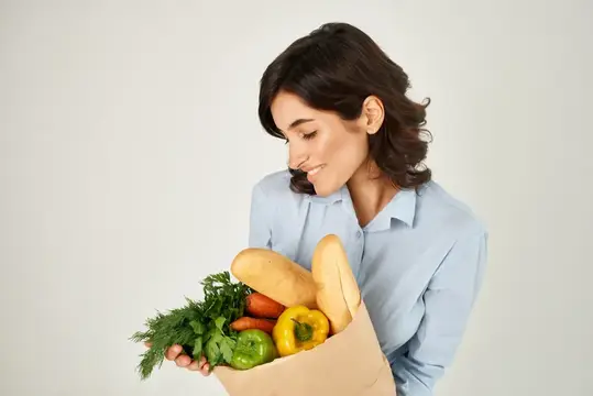 Женщина в голубой рубашке с пакетом овощей и продуктов