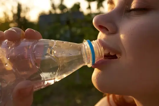 Веселая женщина пьет воду из бутылки летом, крупный план