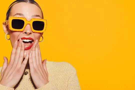 Удивленная женщина в желтых солнцезащитных очках на оранжевом фоне