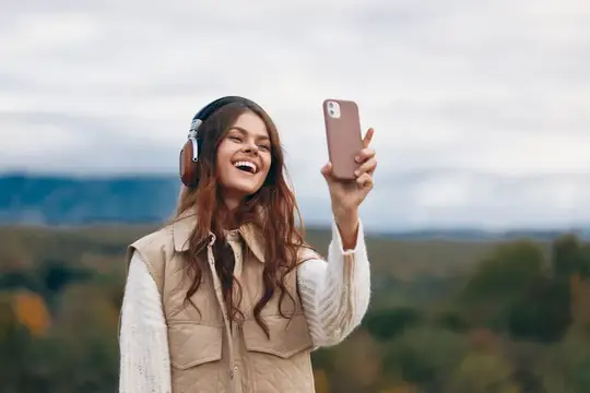 Смеющаяся девушка в наушниках делает селфи на фоне осенних холмов