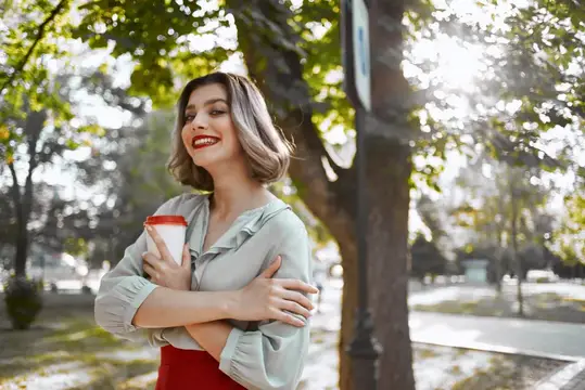 Улыбающаяся женщина с кофе в осеннем парке