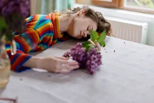 Молодая женщина в ярком свитере лежит на столе с веткой сирени