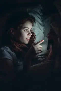 Рыжеволосая девушка ночью в постели смотрит на экран смартфона