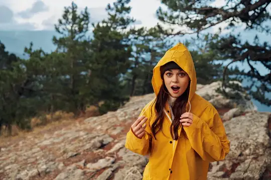 Удивлённая девушка в жёлтом дождевике на скалистой вершине
