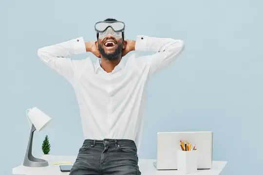 Бородатый мужчина в VR-очках смеётся за рабочим столом