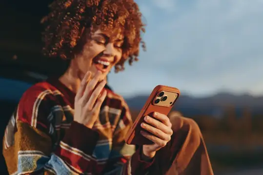 Смеющаяся кудрявая девушка смотрит в смартфон на закате