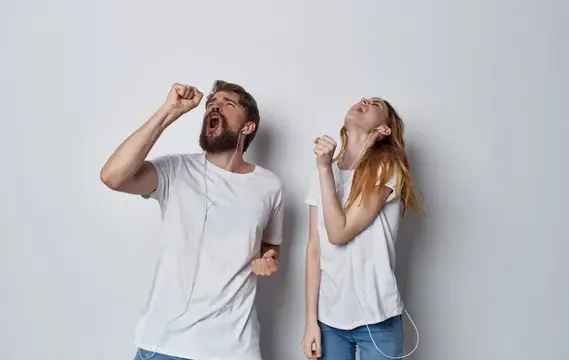 Счастливые друзья в наушниках слушают музыку и танцуют на светлом фоне