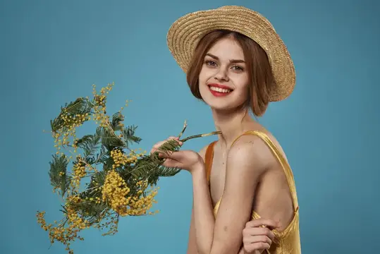 Улыбающаяся девушка в соломенной шляпе с ветками мимозы