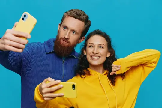 Бородатый мужчина и улыбчивая женщина делают селфи на жёлтые смартфоны