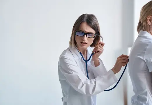 Женщина-врач в очках слушает пациентку стетоскопом