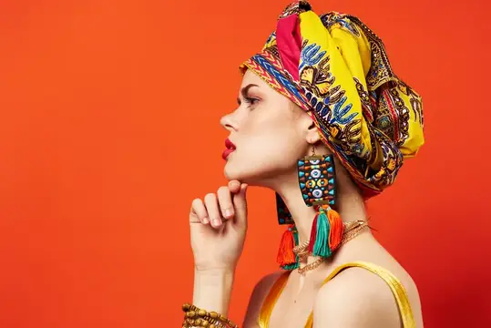 Светлокожая женщина в жёлтом тюрбане и серьгах с кисточками на оранжевом фоне