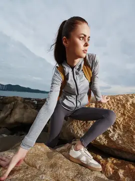Спортивная молодая женщина в серой спортивной одежде позирует на каменистой местности, отражая силу и решительность на фоне спокойного открытого пространства, что идеально подходит для фитнес-тем