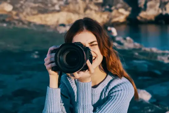 Улыбающаяся девушка фотографирует на камеру у горной реки