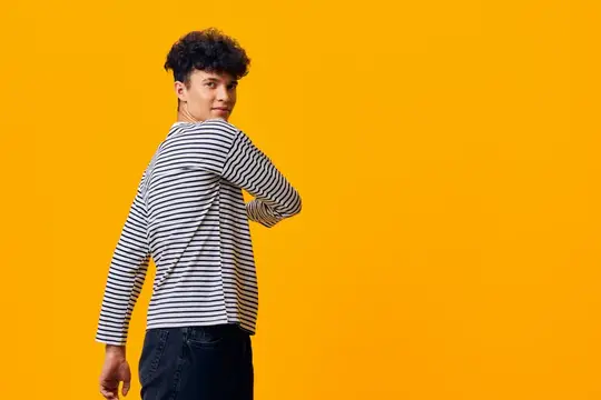 Кудрявый парень в полосатой футболке обернулся на жёлтом фоне