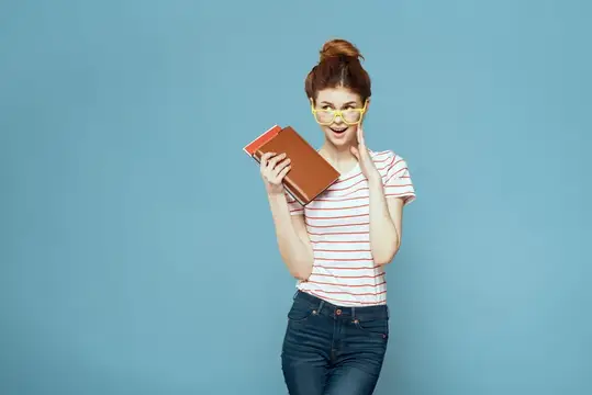 Рыжеволосая девушка в жёлтых очках с книгой на голубом фоне