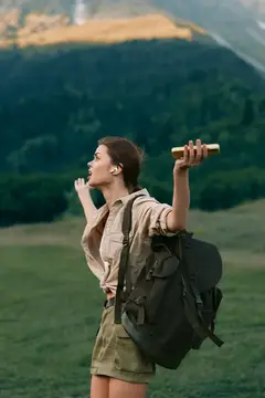 Девушка с рюкзаком пьёт воду на фоне зелёных гор