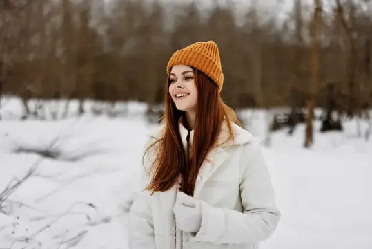 Улыбающаяся девушка в оранжевой шапке на зимней прогулке