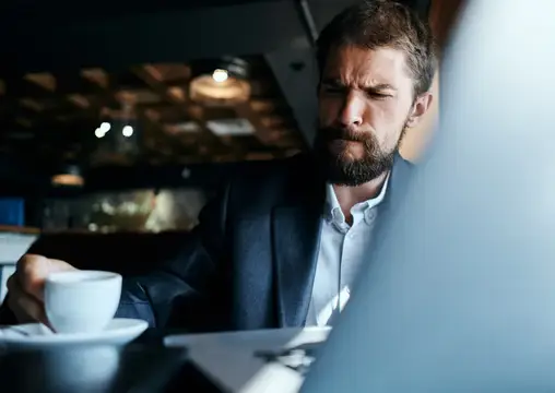 Серьёзный бородатый мужчина в пиджаке с чашкой кофе в кафе