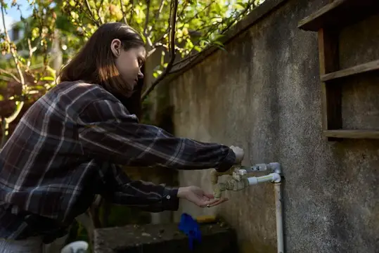 Девушка в клетчатой рубашке набирает воду из уличного крана