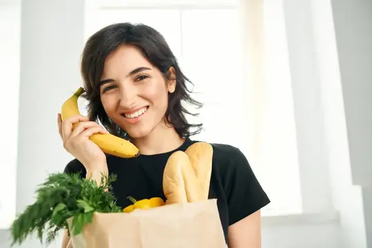 Жизнерадостная женщина с пакетом продуктов на кухне