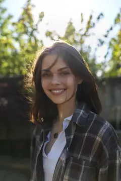 Улыбающаяся темноволосая девушка в клетчатой рубашке на закате