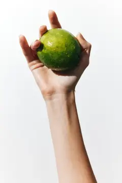 Рука держит спелый зелёный лайм на белом фоне