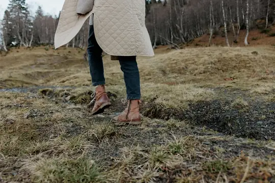 Женские ноги в осенней одежде ступают по земле на фоне лесного пейзажа