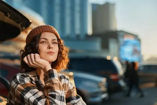Молодая женщина в клетчатой рубашке и шапке у машины в городе