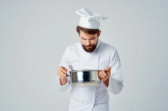 Мужчина в поварской форме с кастрюлей в руках пробует еду в ресторане