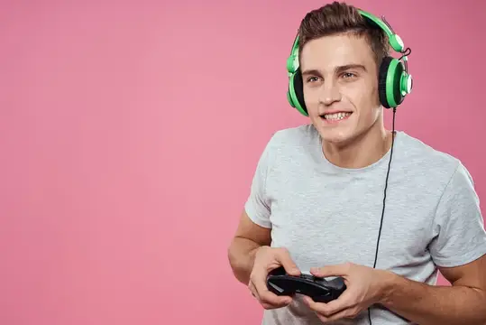 Улыбающийся парень в наушниках играет в видеоигру на розовом фоне