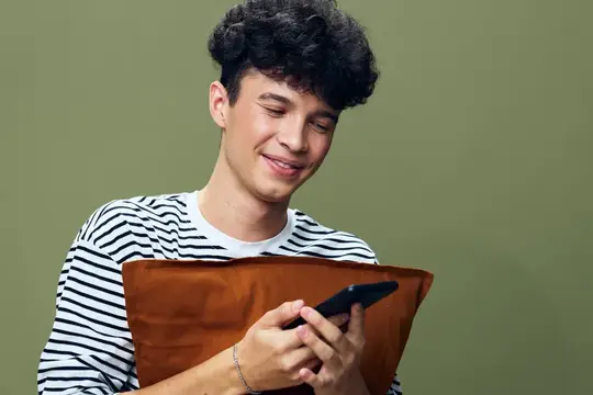 Улыбающийся парень с кудрявыми волосами смотрит в смартфон на зелёном фоне