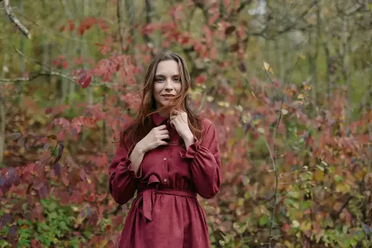 Молодая женщина в бордовом платье стоит в осеннем лесу