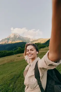Улыбающаяся девушка с рюкзаком делает селфи на фоне гор