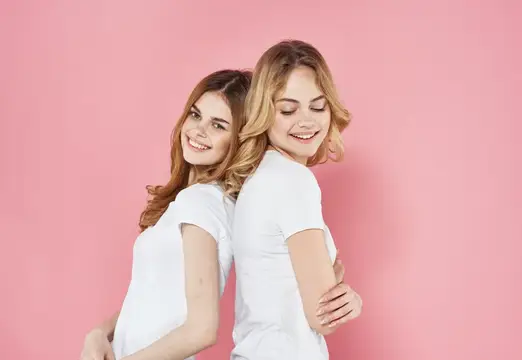 Две улыбающиеся девушки в белых футболках на розовом фоне