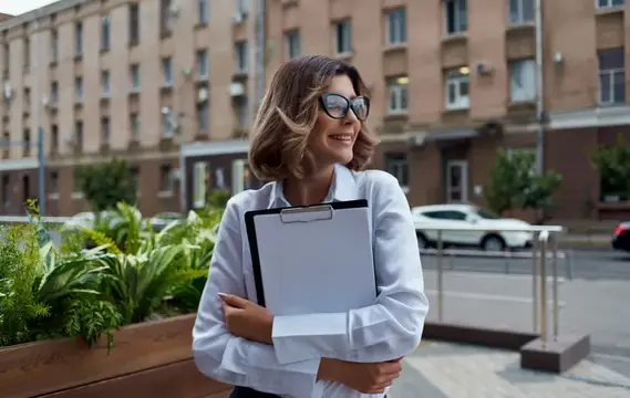 Женщина на улице возле цветов показывает документы в папке